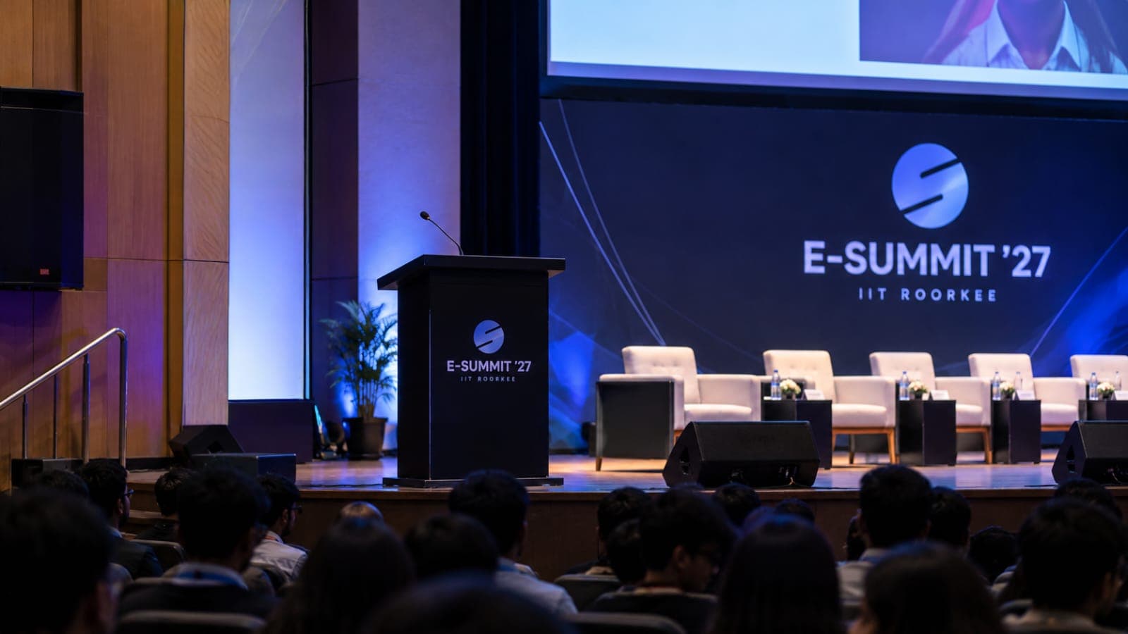 An E-Summit ’27 podium with a microphone on a spotlit stage